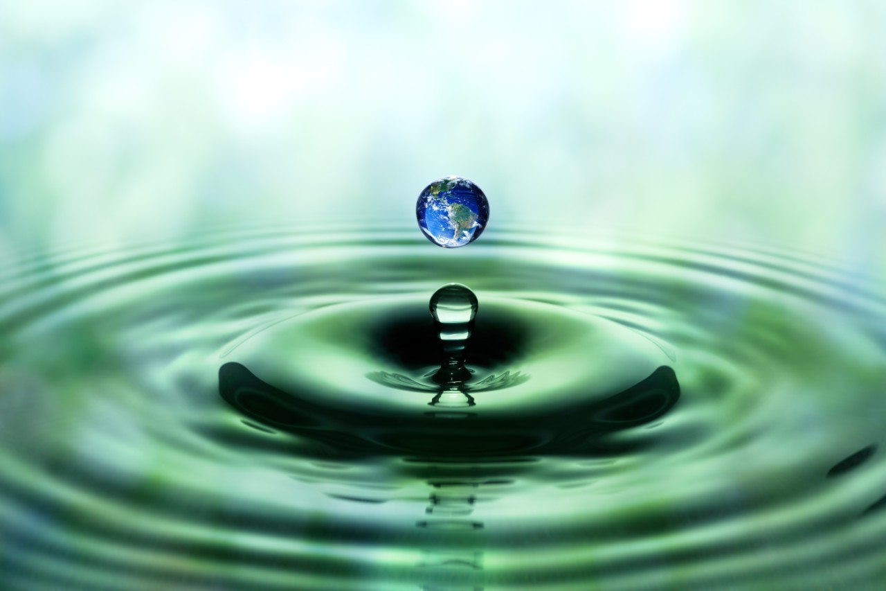 Drop of rain with blue earth image falling on smooth water surface. Green blurred pattern in background.